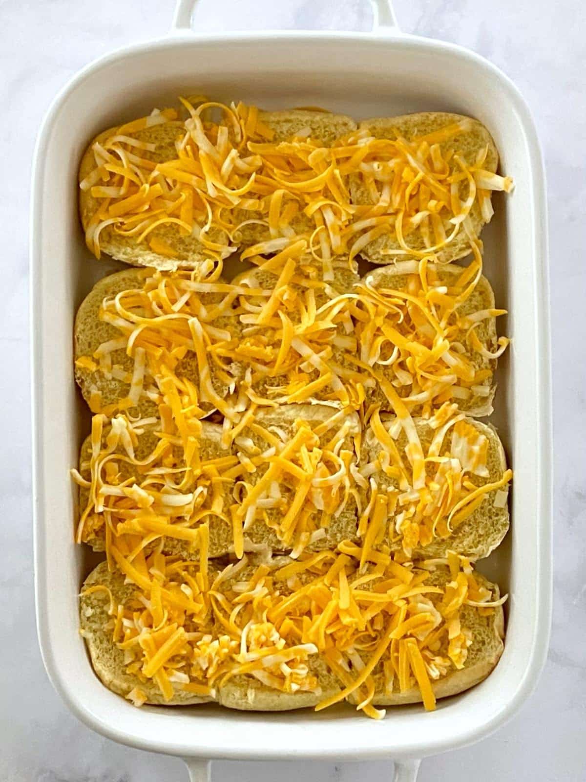 Slider rolls topped with cheese in a baking dish.
