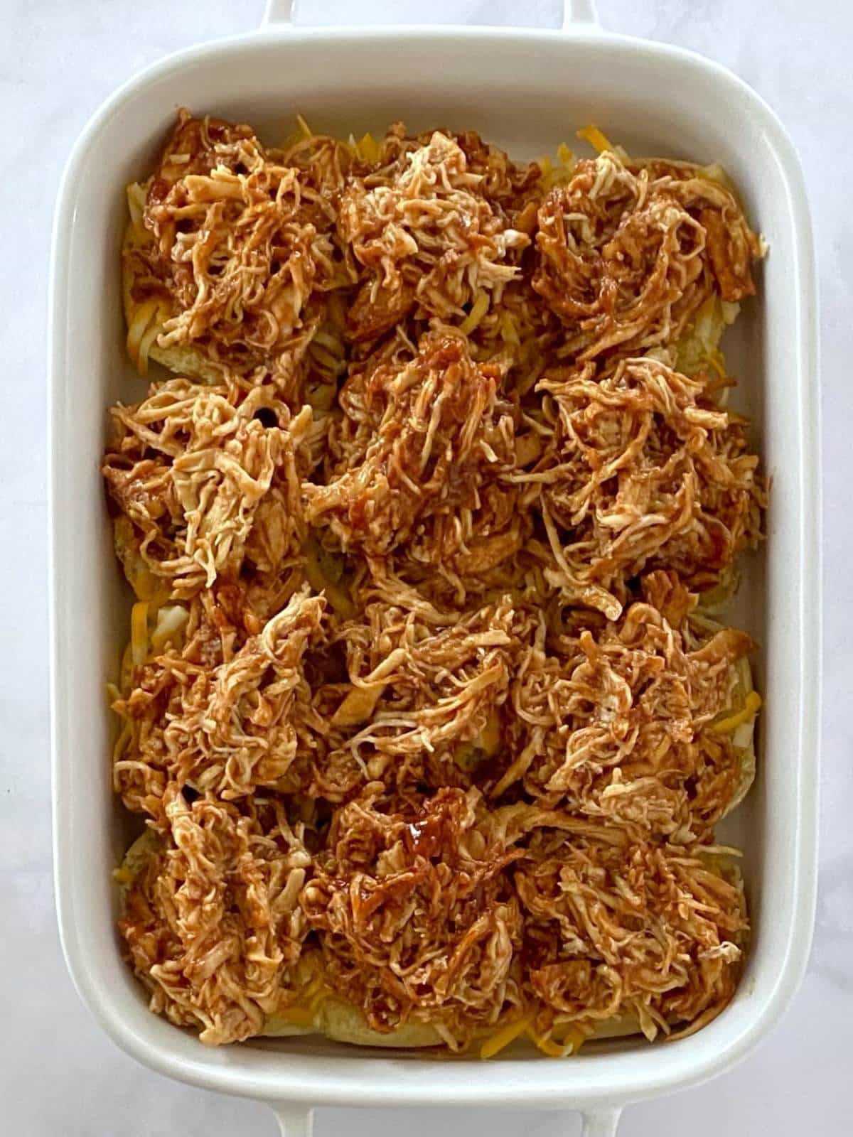 Slider rolls with cheese and bbq chicken in a baking dish.