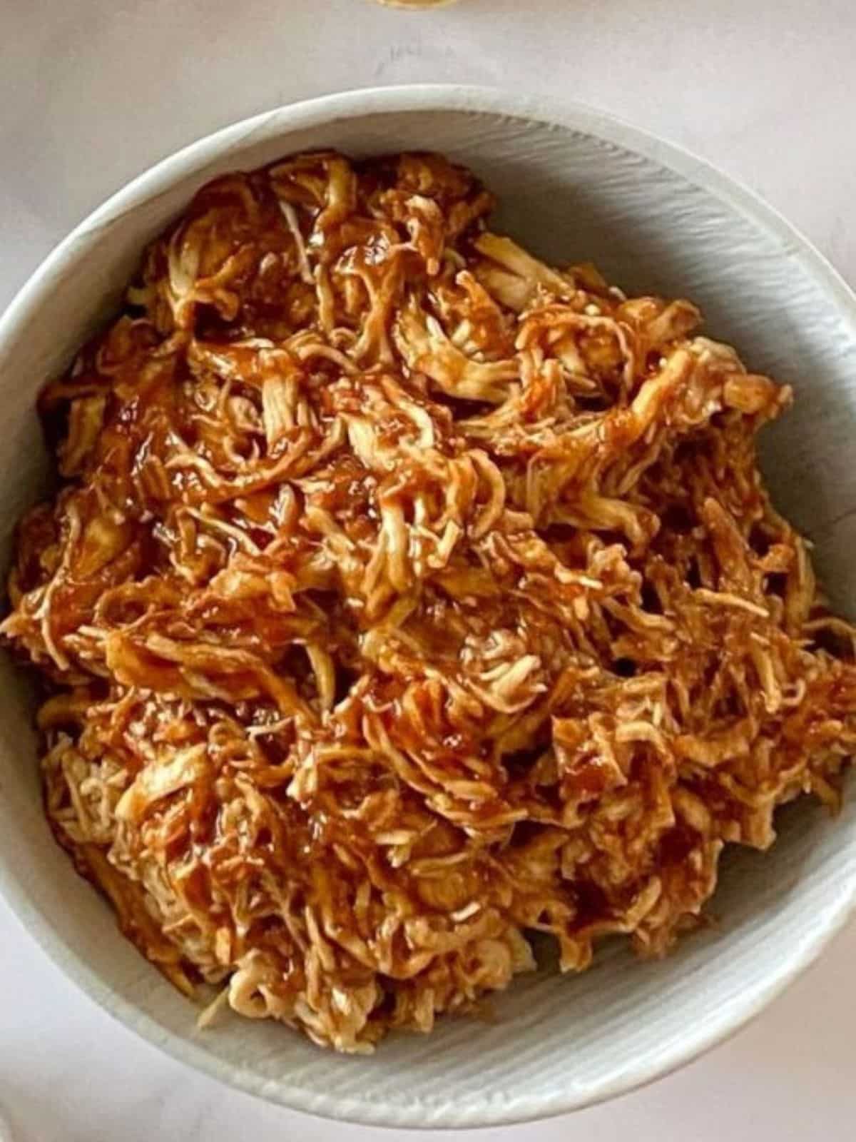 A bowl of shredded chicken mixed with barbecue sauce.