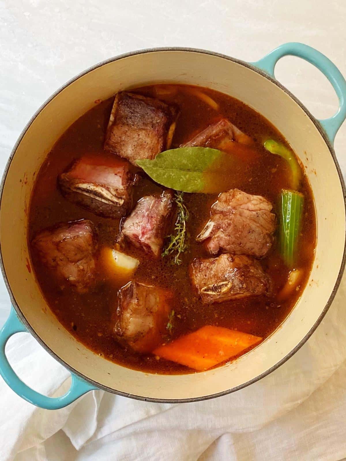 Short ribs, vegetables, and short ribs in a Dutch oven.