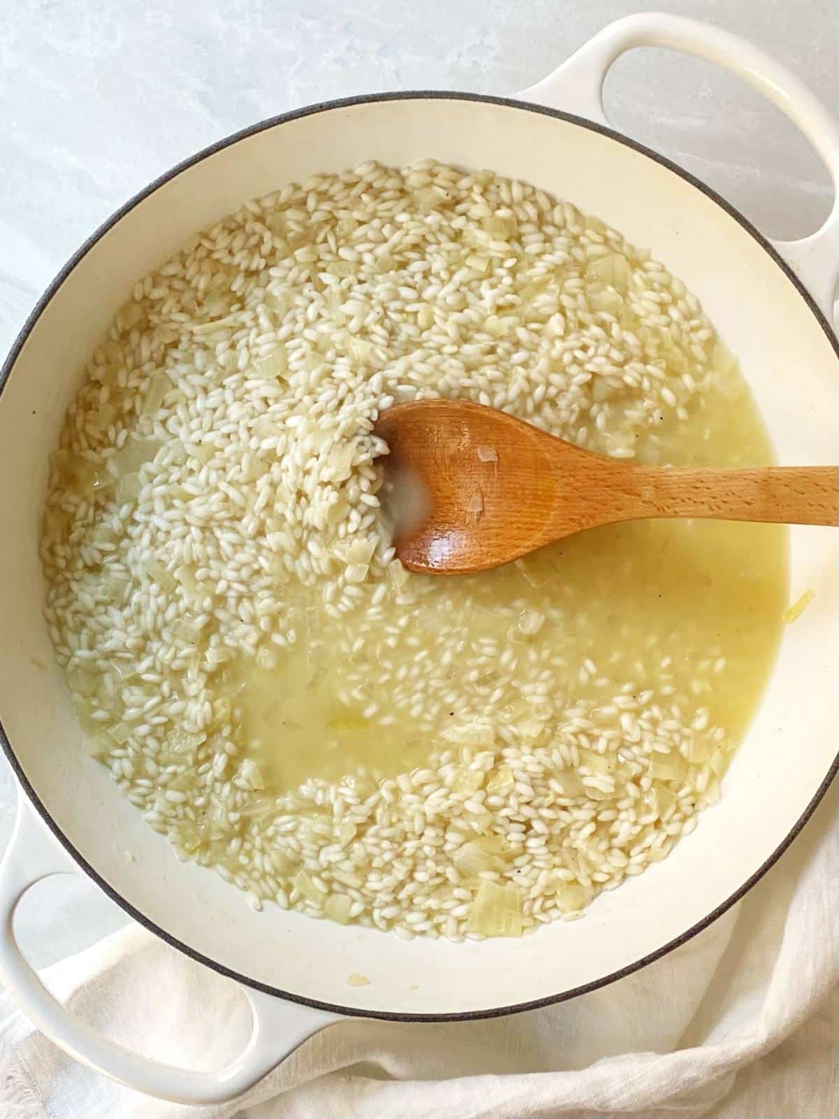 Adding broth to the risotto in a skillet.