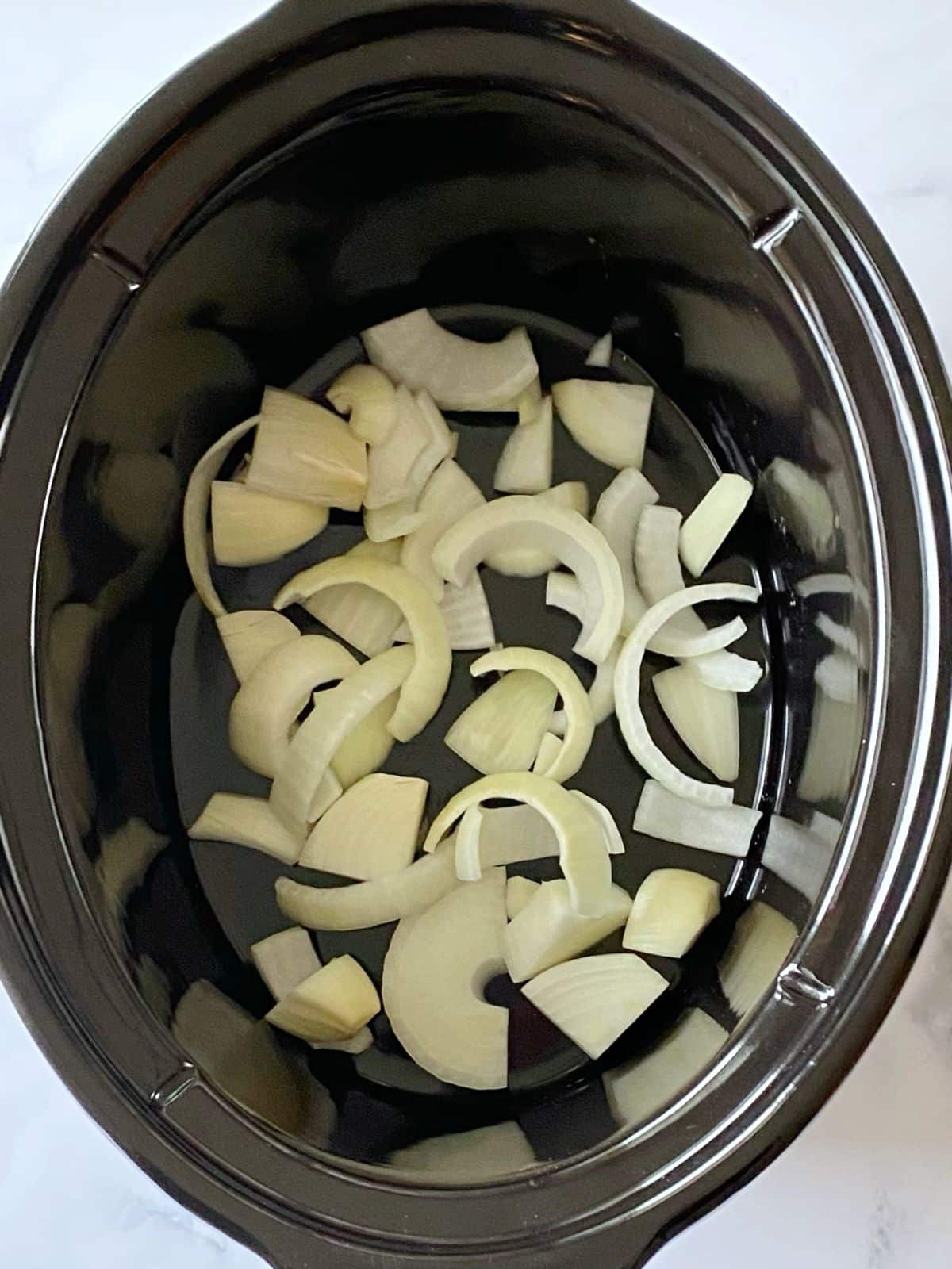 Sliced onions in bottom of slow cooker.