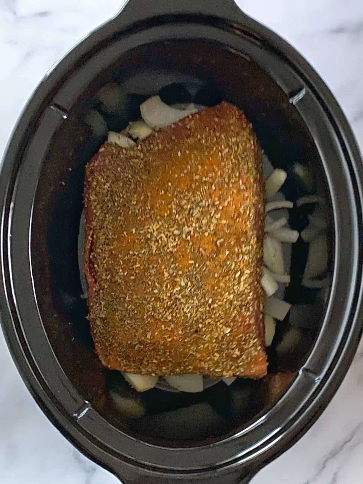 Brisket placed on top of onions in slow cooker.