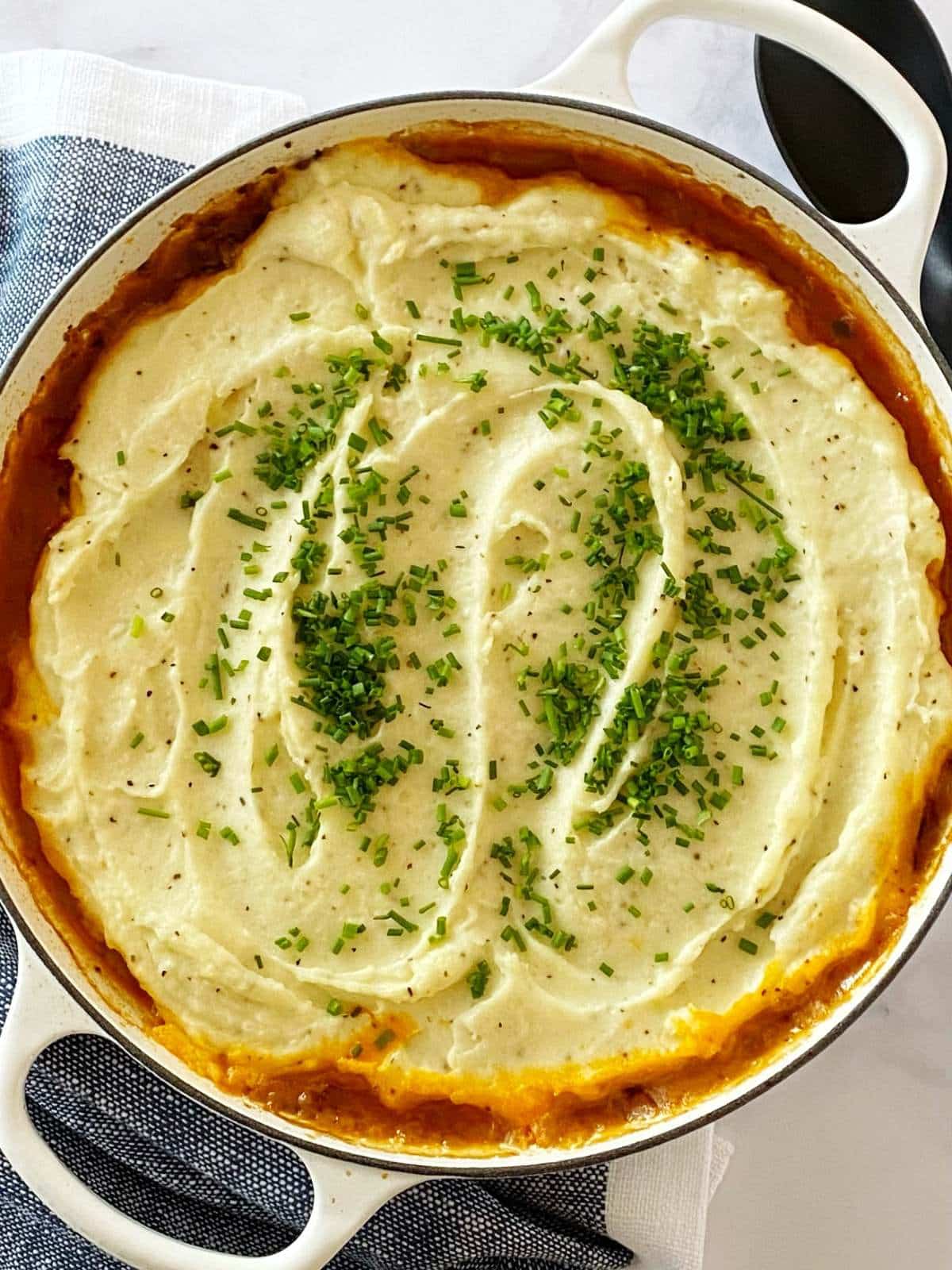 Casserole dish of meat and potatoes topped with chopped chives.