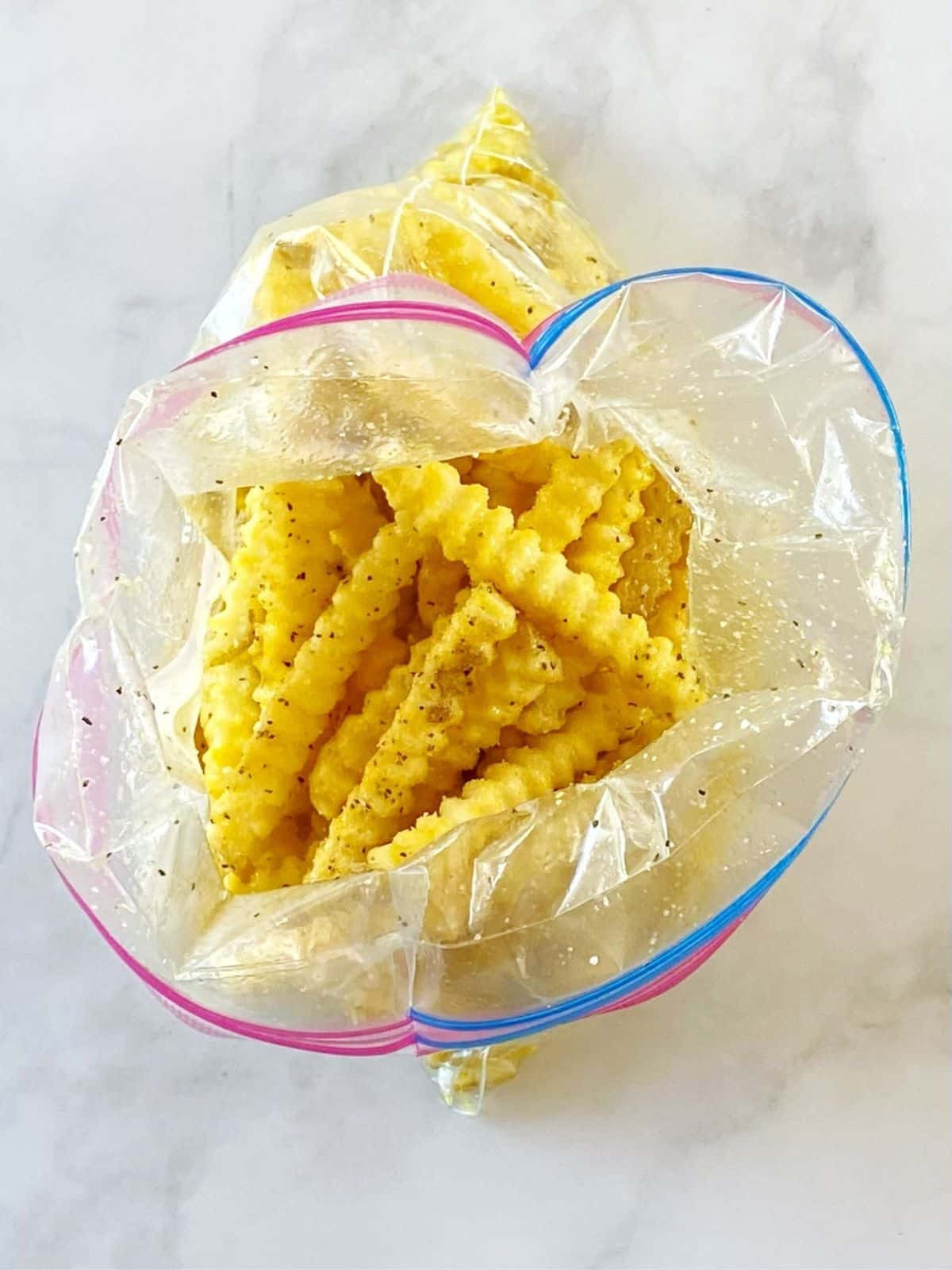 French fries tossed with oil and seasonings in a zipper-top bag.