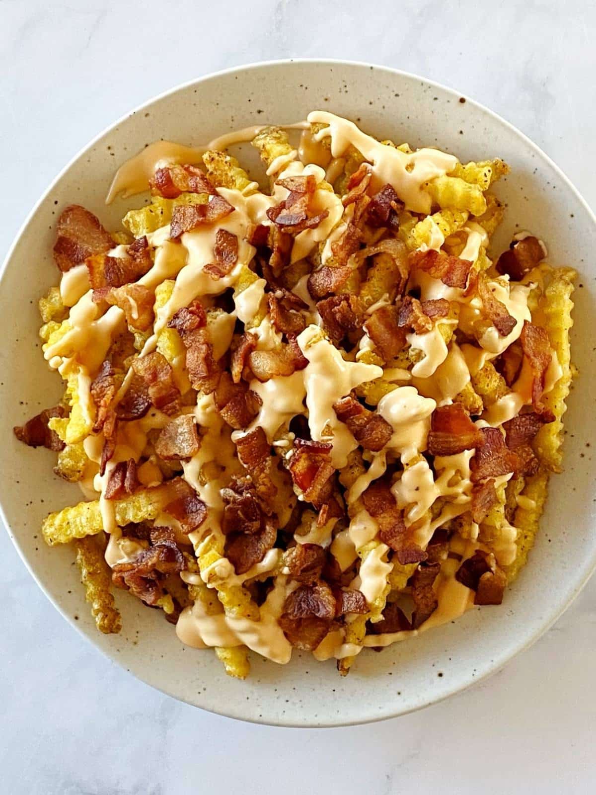 Two layers of fries, cheese sauce, and bacon on a serving plate.