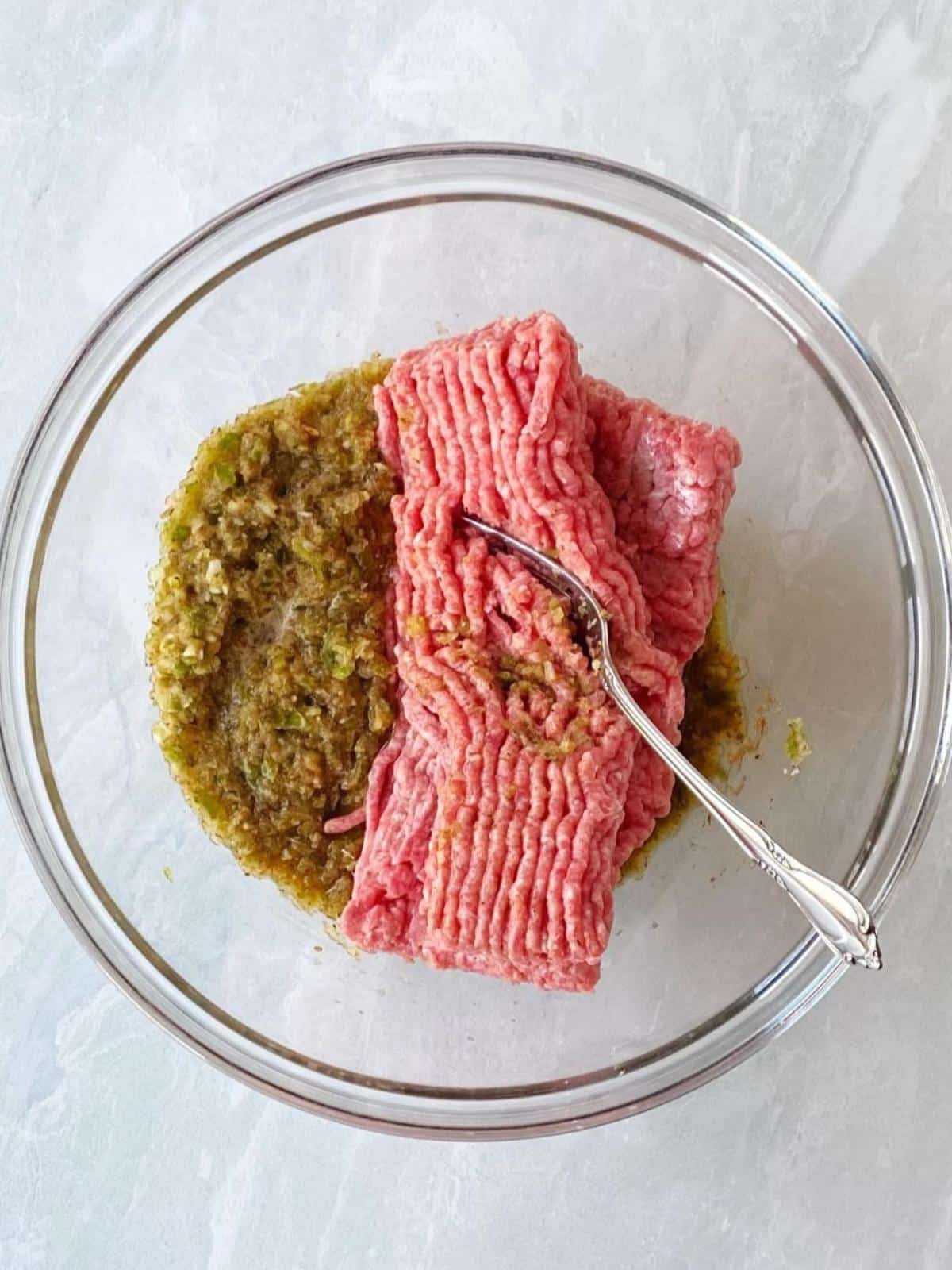 Ground meat with pepper and onion mixture in a mixing bowl.