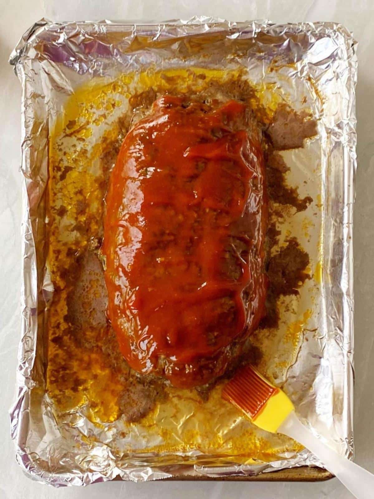 Meatloaf topped with glaze on a sheet pan.