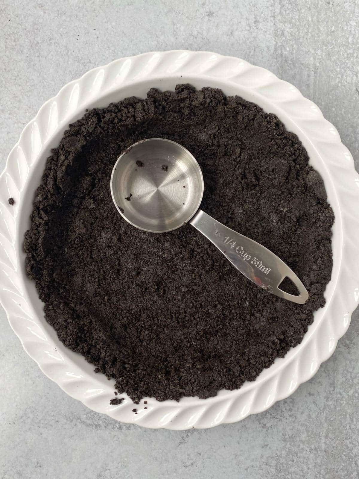 Pressing cookie crumb mixture into a pie dish with a metal measuring cup.