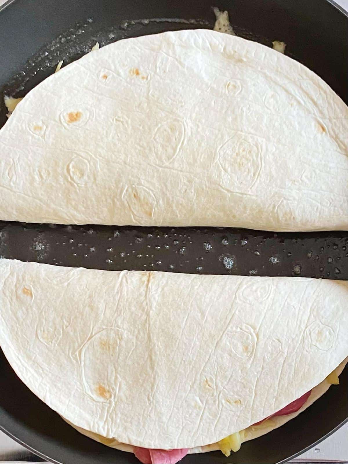Quesadillas folded in half cooking in a skillet.