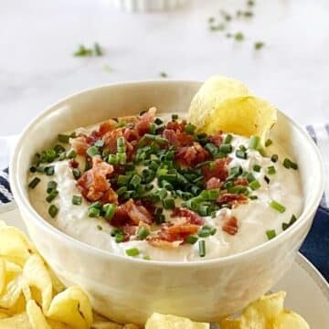 Bacon horseradish dip garnished with chives in a bowl with potato chips.