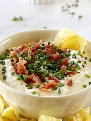 Bacon horseradish dip garnished with chives in a bowl with potato chips.