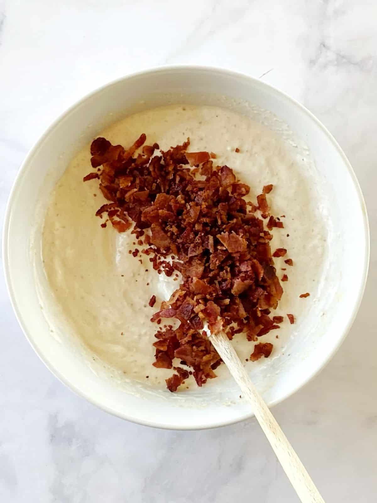 Stirring bacon into a bowl of dip.