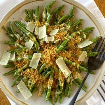 Beans with dressing, breadcrumbs, and Parmesan shavings on a platter with a serving fork.