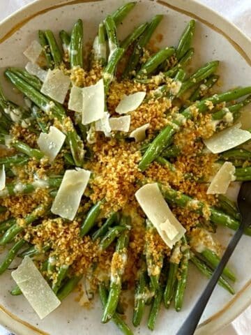 Beans with dressing, breadcrumbs, and Parmesan shavings on a platter with a serving fork.
