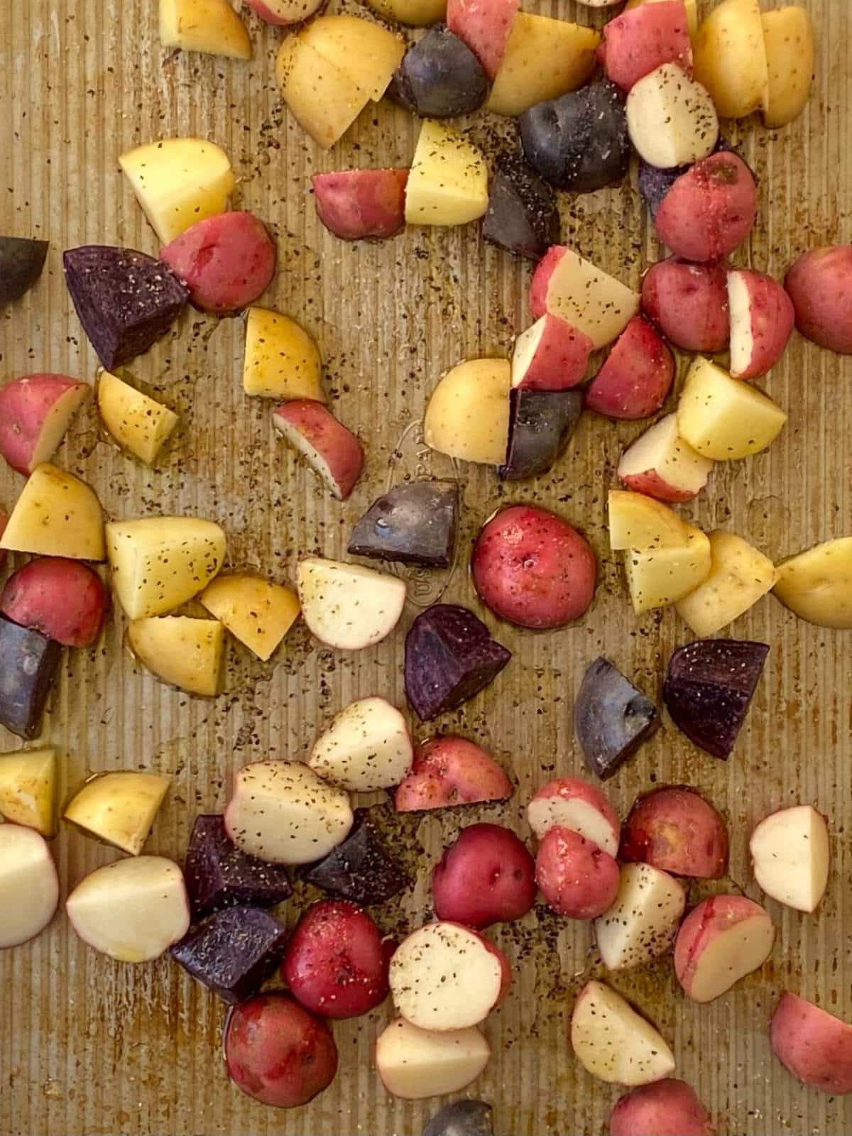 Diced potatoes on a sheet pan tossed with oil and seasonings.