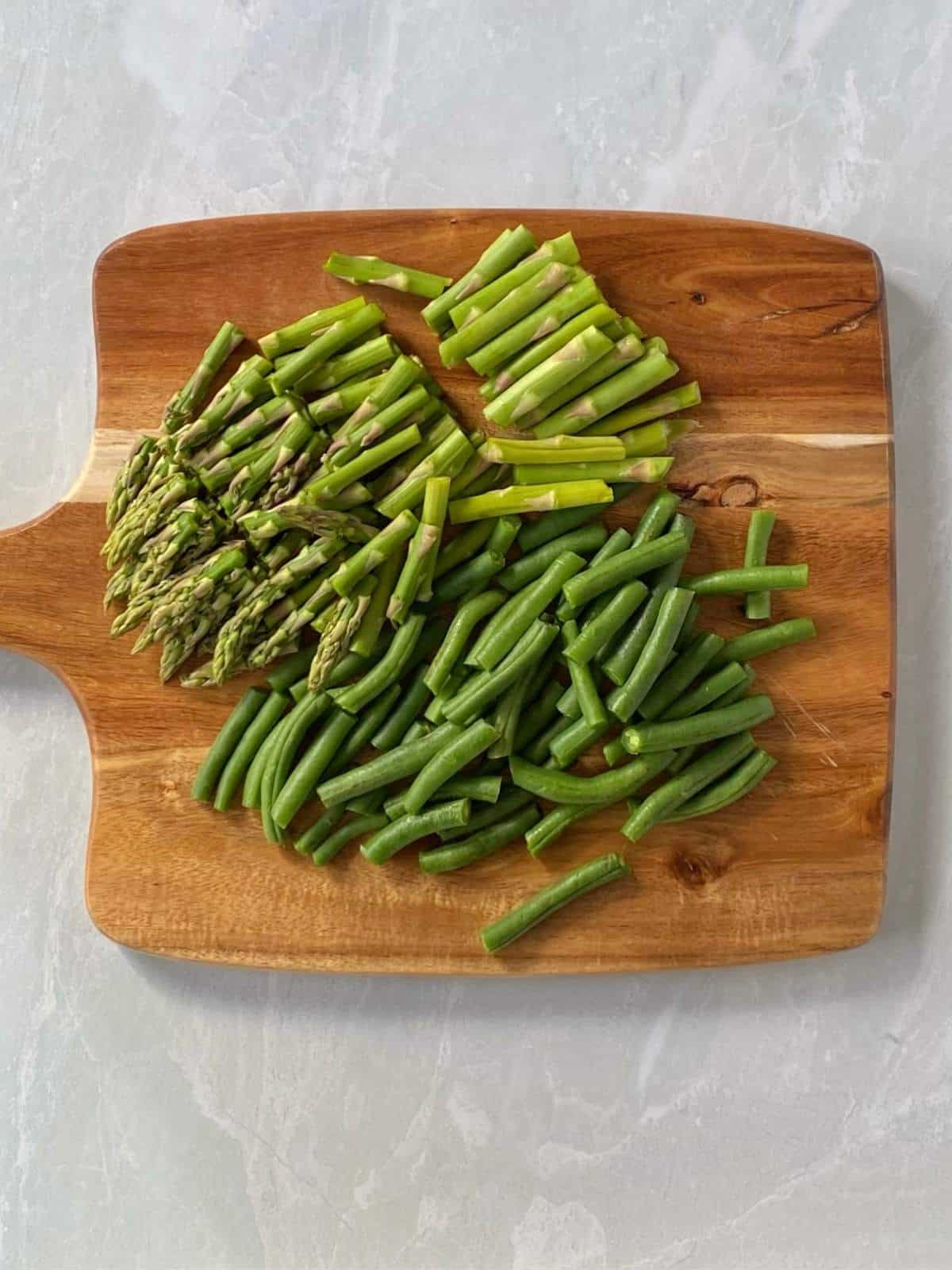 Trimmed and cut asparagus and green beans on a cutting board.
