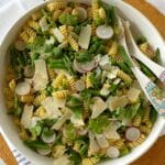 Serving utensils in a bowl of pasta salad.
