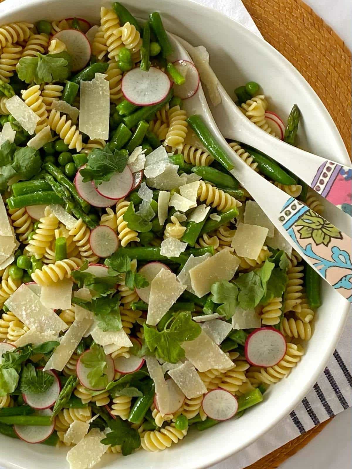 Pasta salad in a white serving bowl with serving spoons.