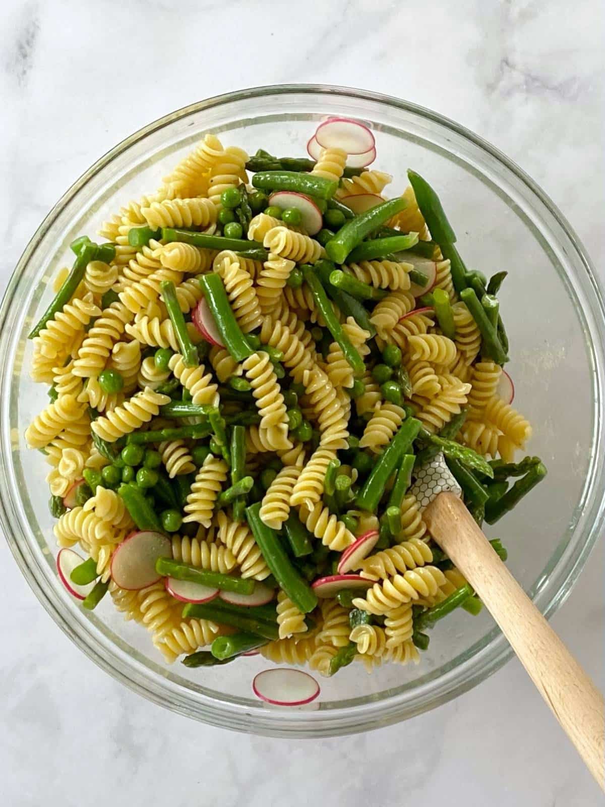 Pasta and veggies tossed with dressing in a mixing bowl.