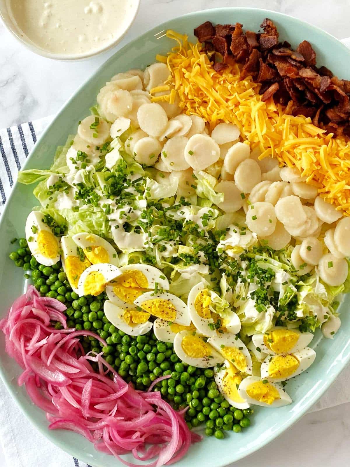 Platter of layered salad ingredients next to a bowl of dressing.