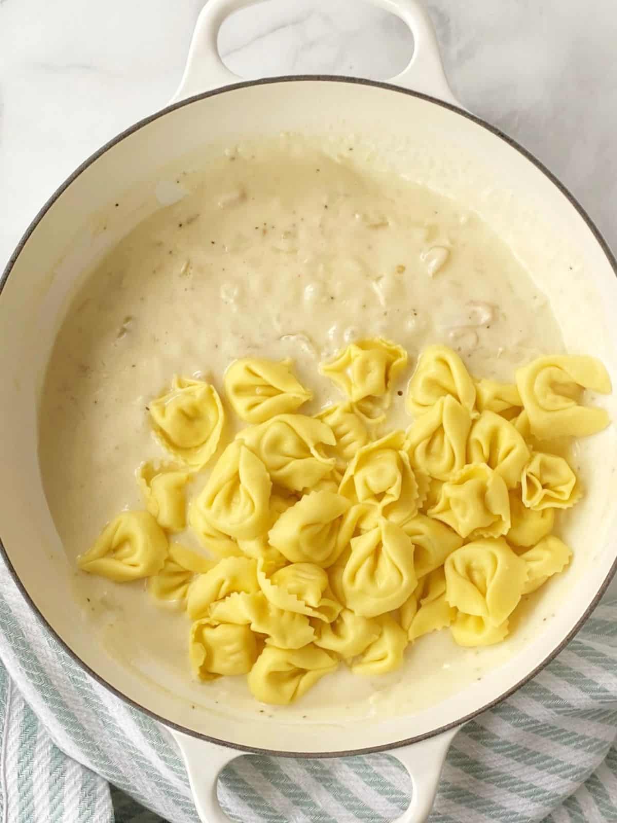 Adding tortellini to the cheesy sauce.