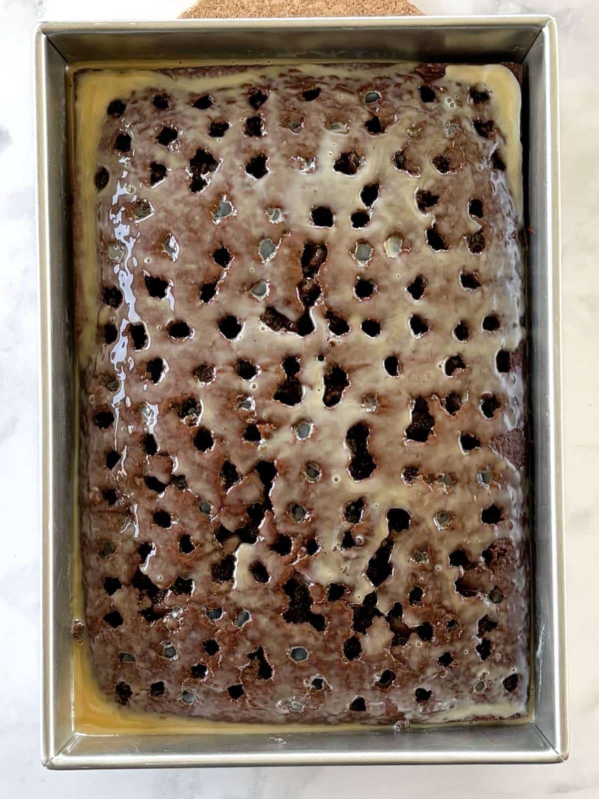 Holes poked in the baked cake with sweetened condensed milk and caramel poured over the top.