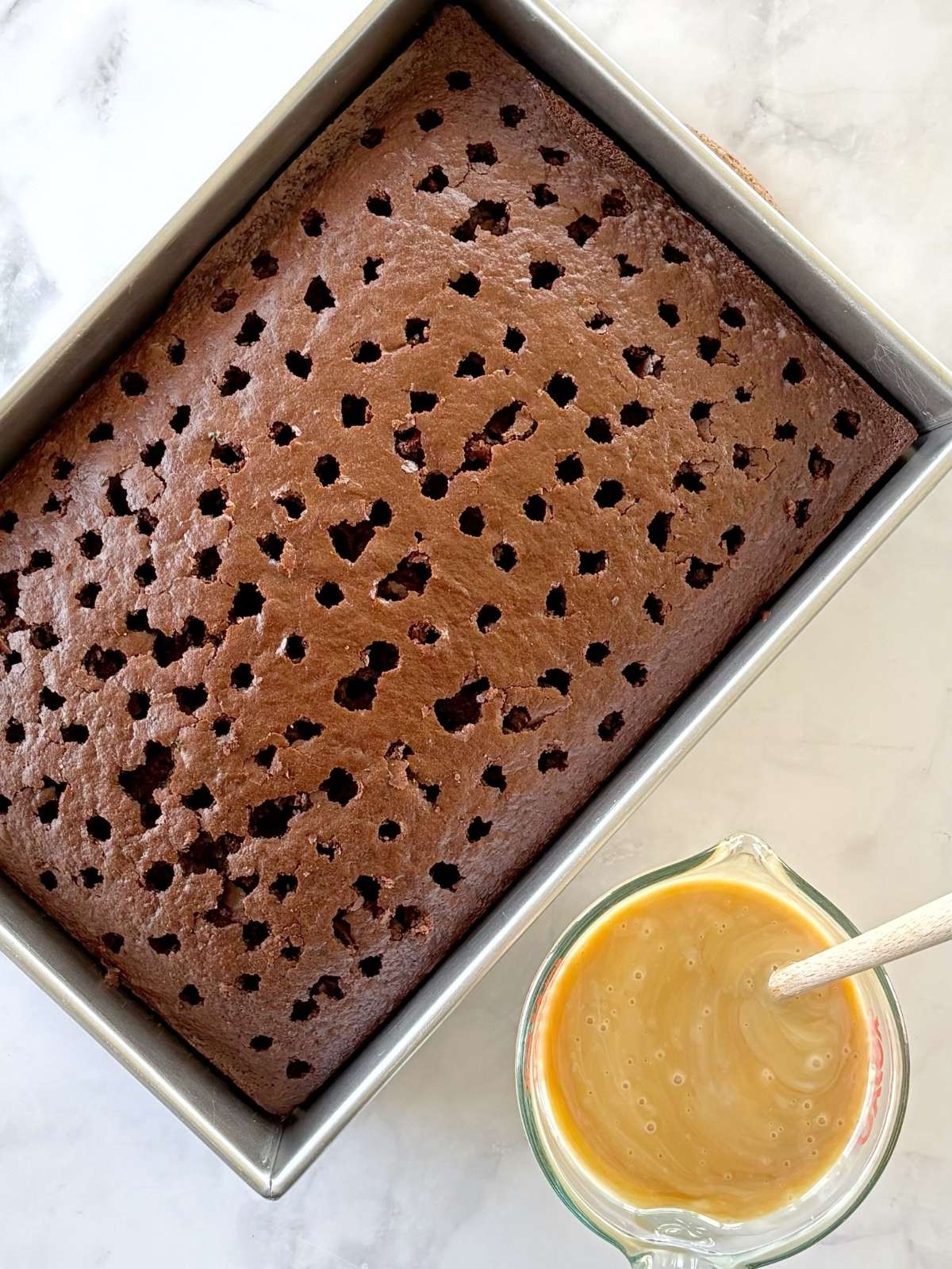 Baked cake with holes poked in the top next to a bowl of the soaking mixture.