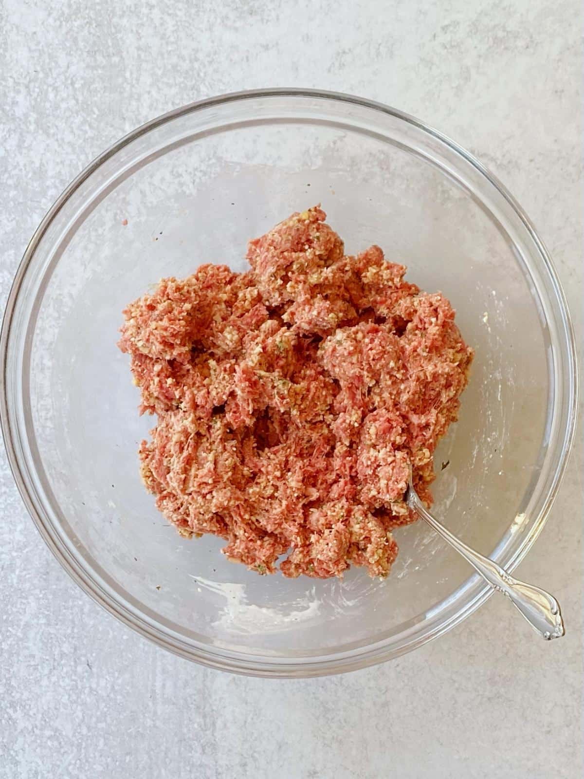 Mixing the beef into the other meatball ingredients.