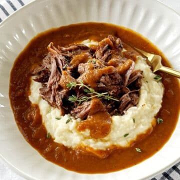 A bowl of potatoes and pot roast with gravy.