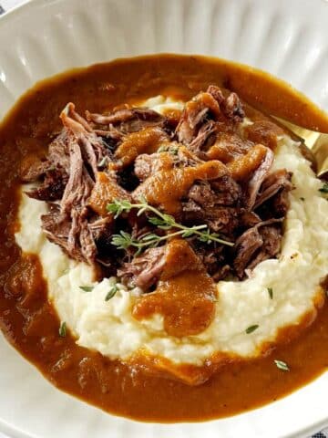 A bowl of potatoes and pot roast with gravy.