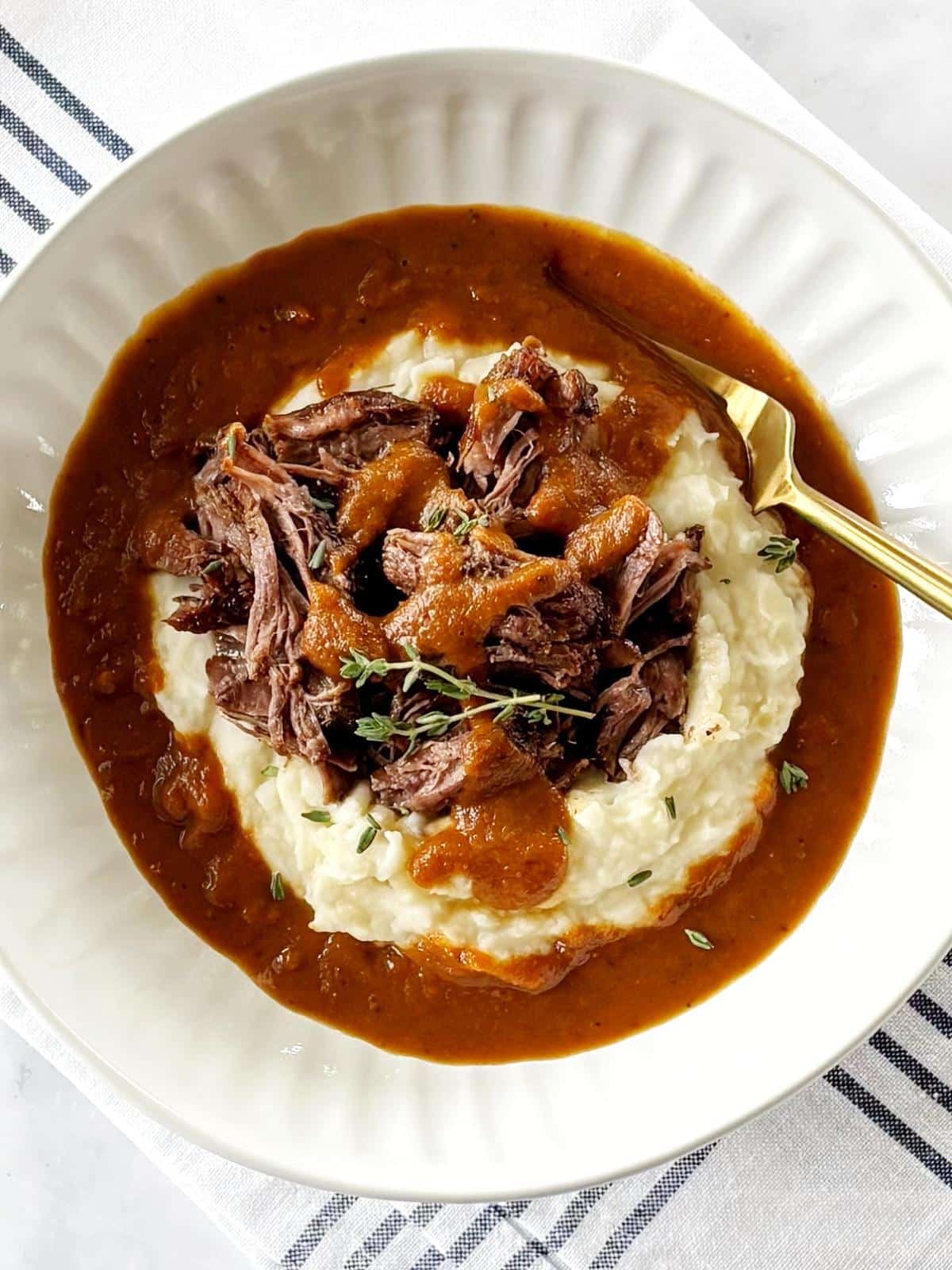A bowl of pot roast,gravy, and mashed potatoes.