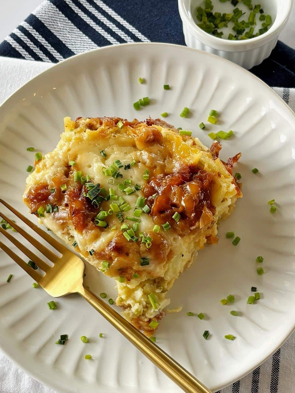 Sausage casserole with hashbrowns on a plate next to a dish of chives.