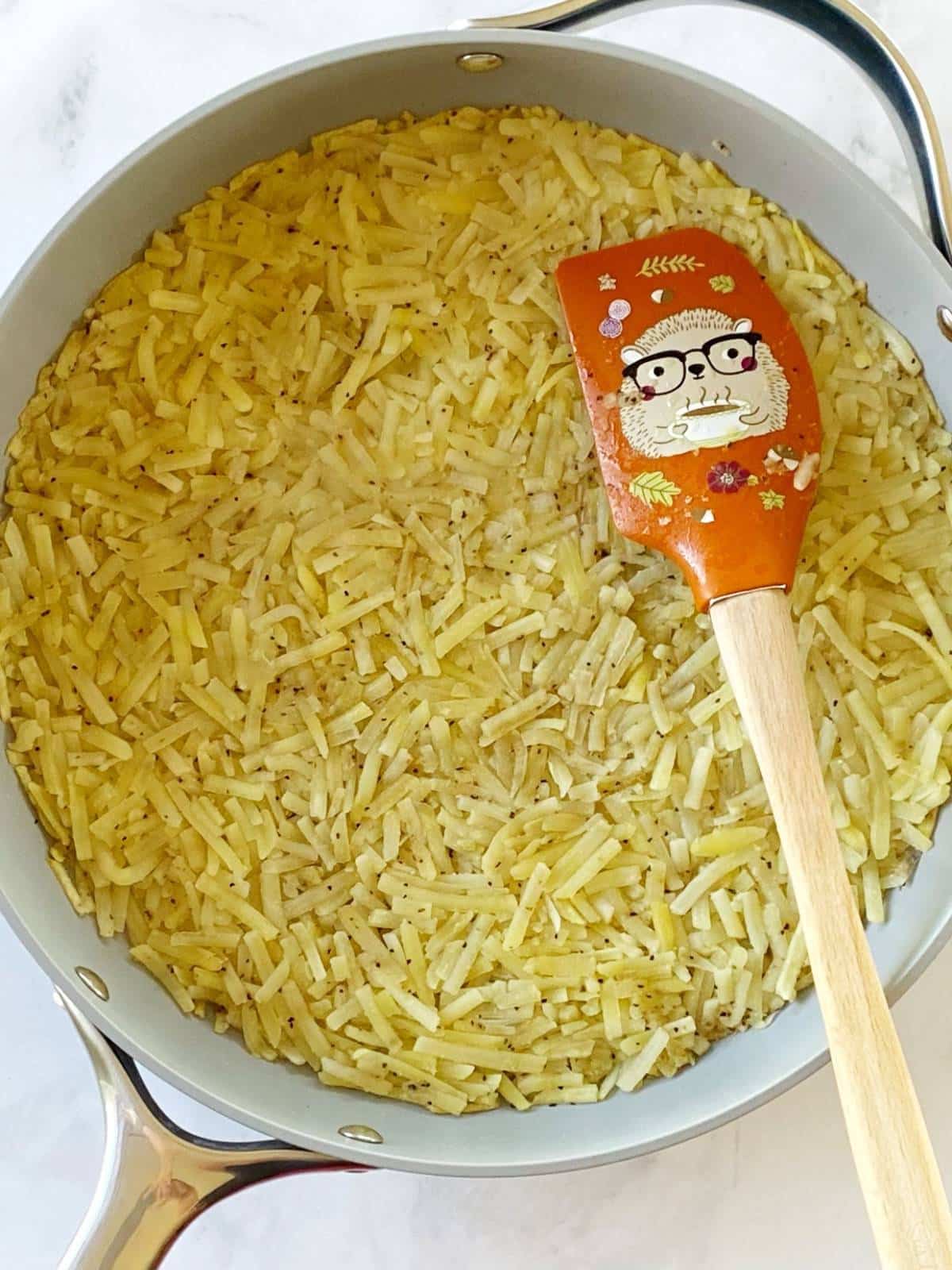 Shredded potatoes pressed into a non-stick skillet.