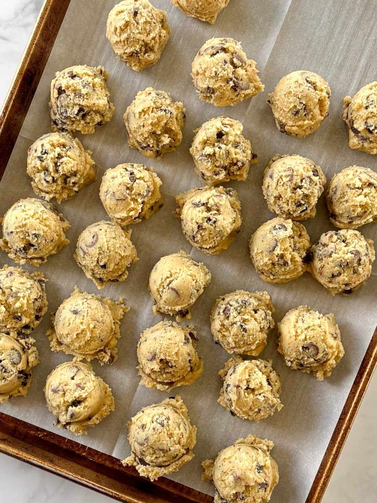 Balls of cookie dough on a parchment-lined sheet pan.