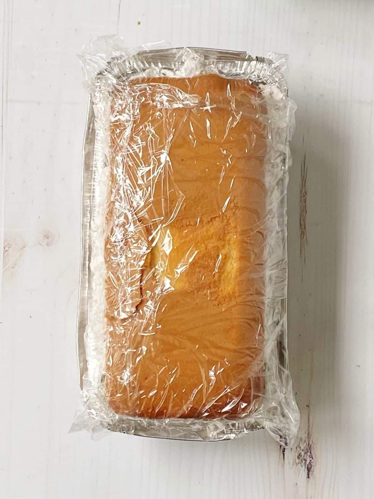 Assembled cake in pan wrapped in plastic wrap.