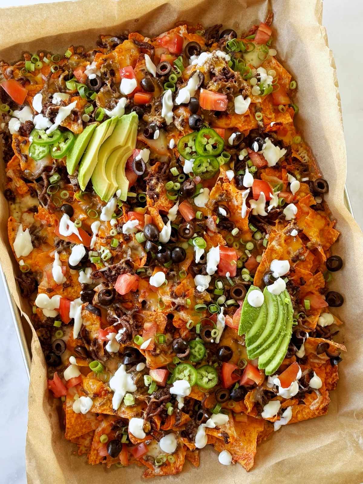 A sheet pan of nachos topped with avocado, scallions, and crema.