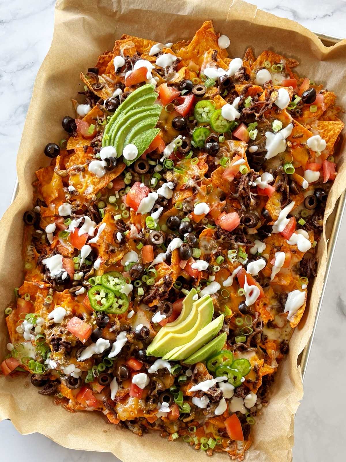 A sheet pan of nachos topped with a variety of garnishes.