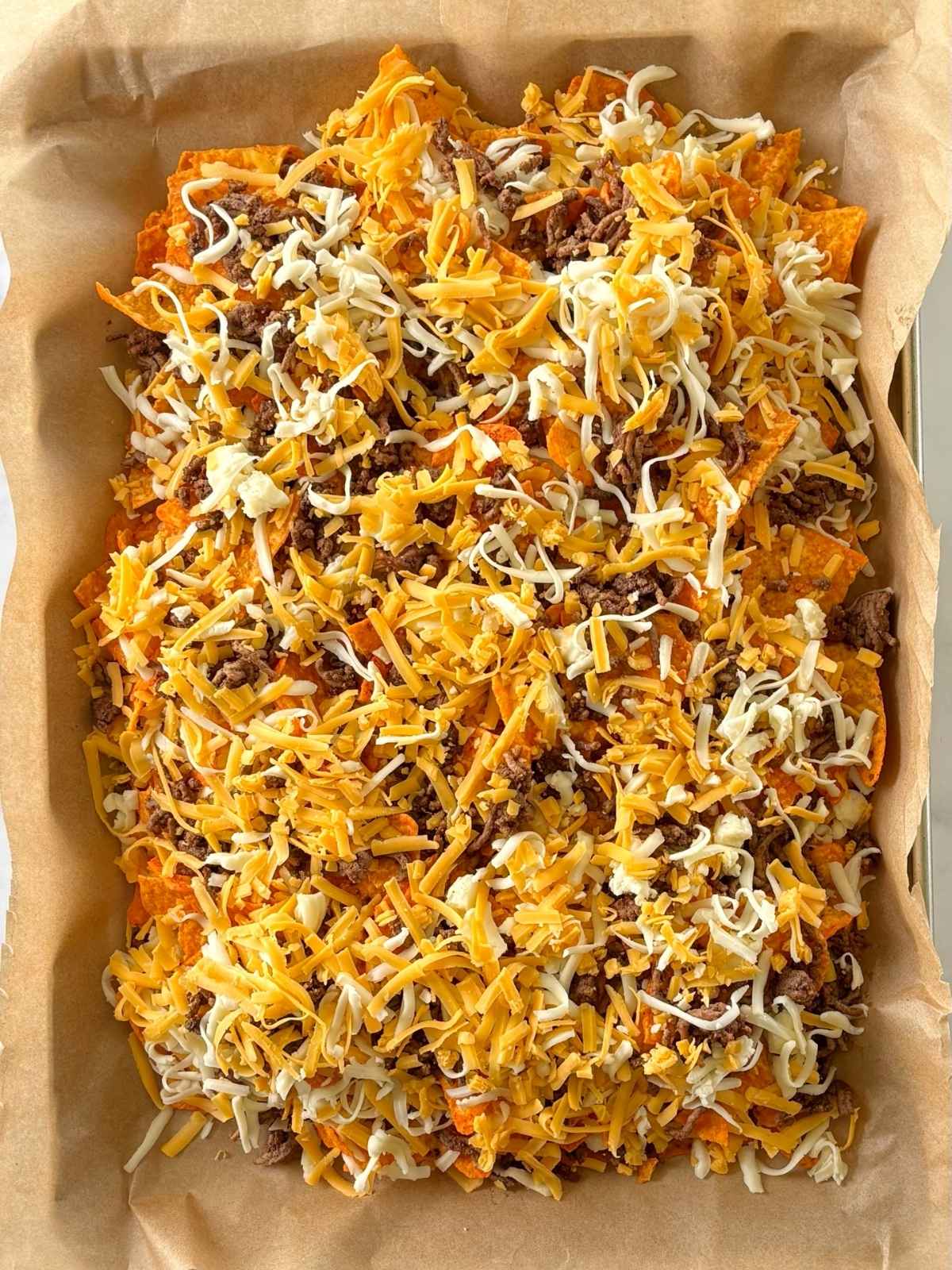 Doritos layered with beef and cheese on a sheet pan.