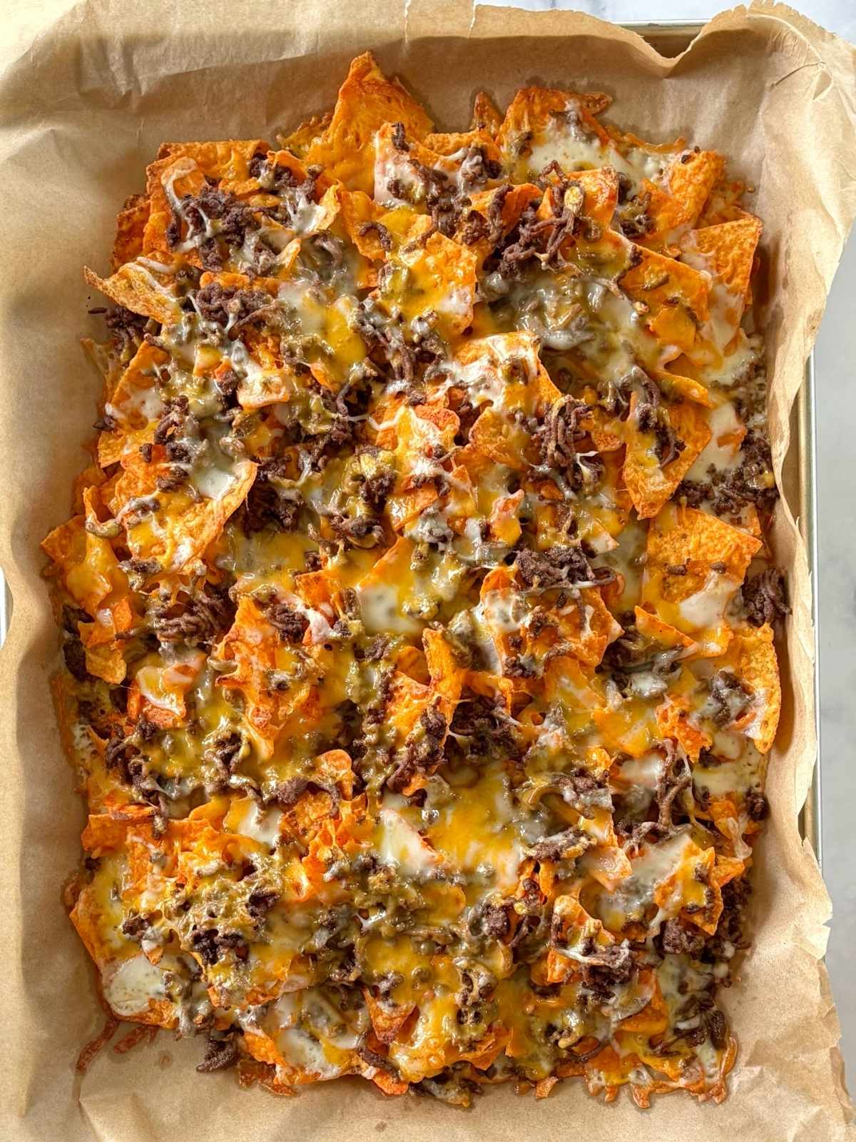 A sheet pan of Doritos, beef, and melted cheese.