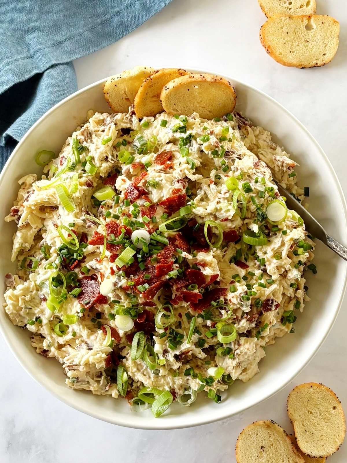 A serving dish of pepperoni dip with a spreader and some bagel chips.