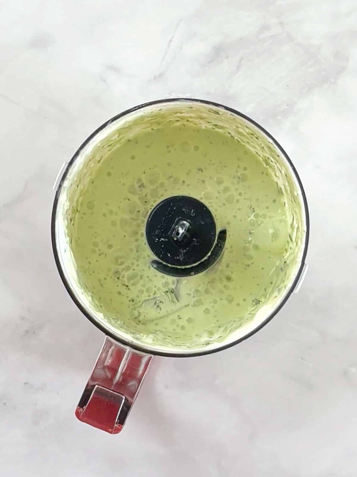 Jalapeno, lime, and cilantro sour cream mixture in a food processor bowl.