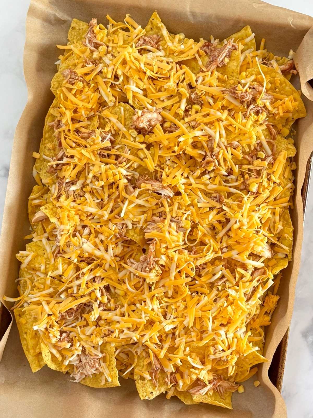 Nachos layered on a sheet pan before baking.