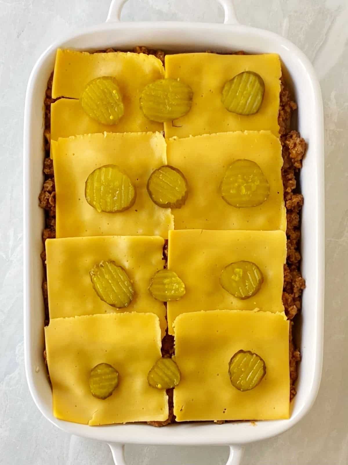 Layering more cheese, then pickles, over the beef mixture.