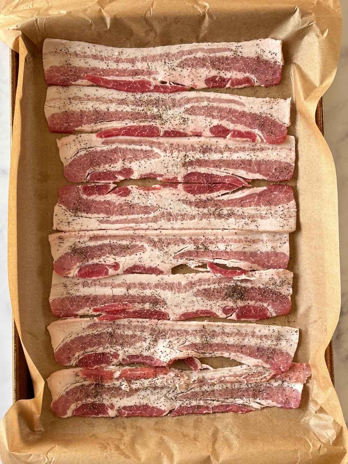Bacon seasoned with pepper on a parchment-lined baking pan.