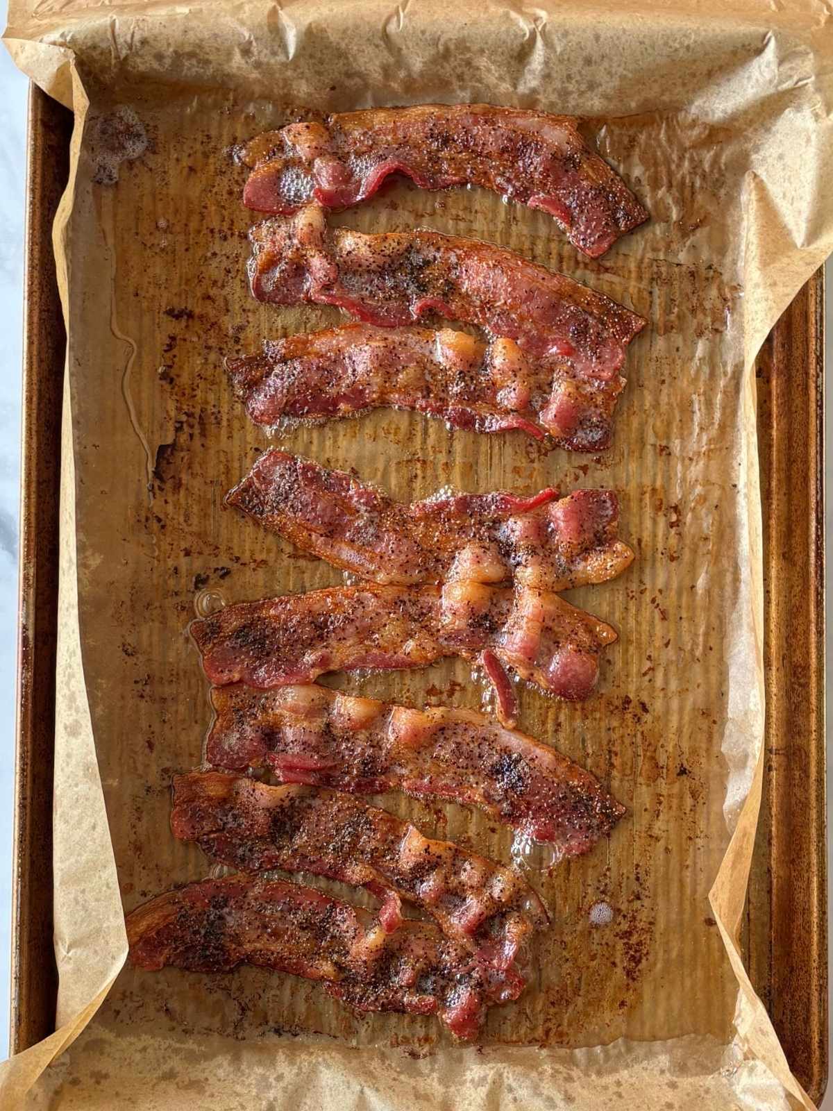 Cooked bacon on a parchment-lined baking pan.