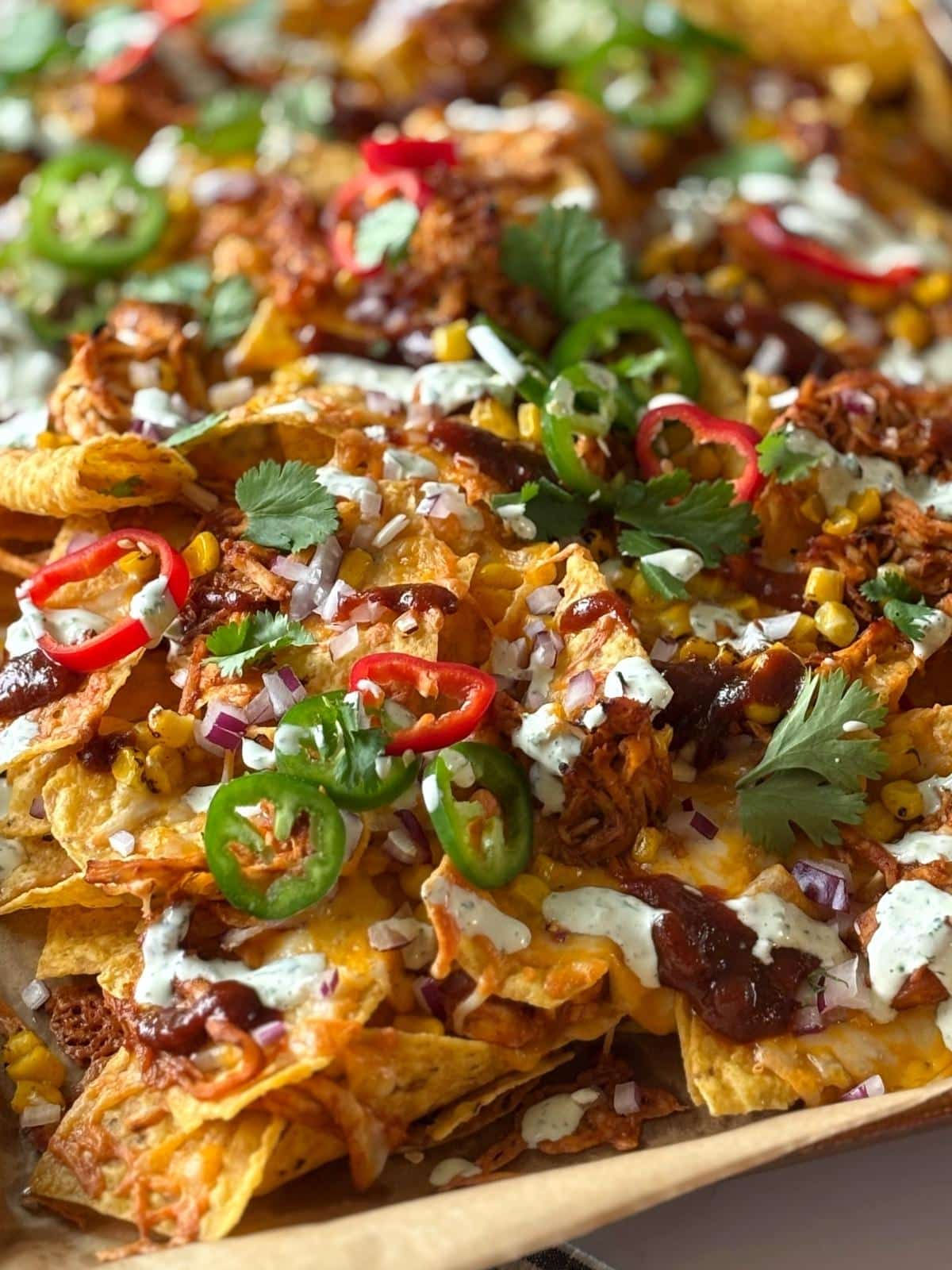 Sheet pan of nachos topped with jalapenos, fresnos, and cilantro.
