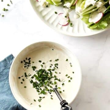 A bowl of blue cheese dressing next to a plate of salad.