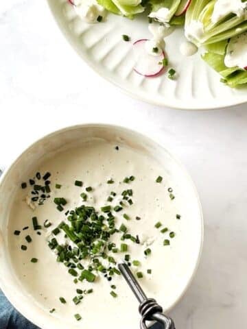 A bowl of blue cheese dressing next to a plate of salad.