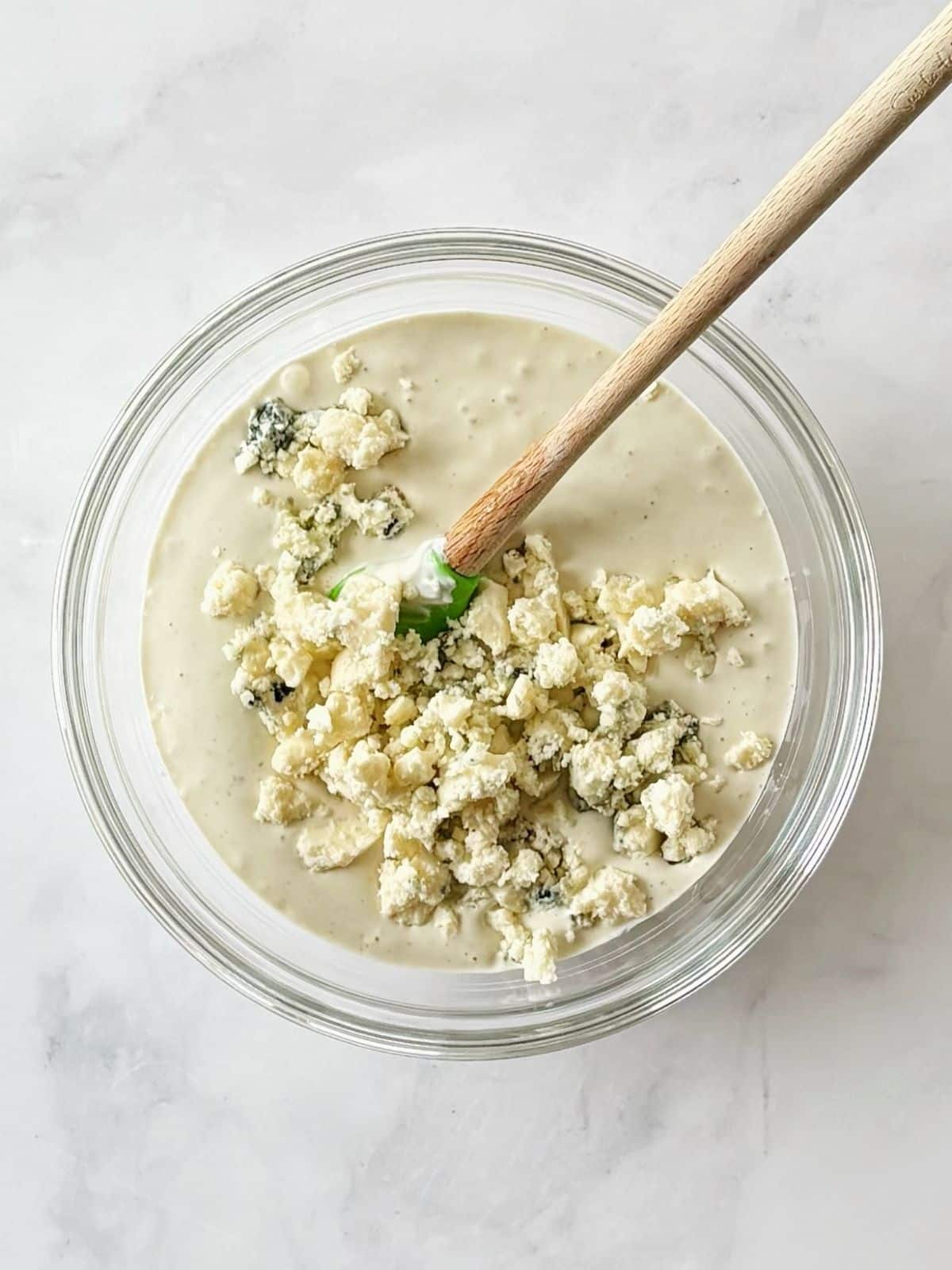 Folding blue cheese crumbles into a bowl of blue cheese dressing.